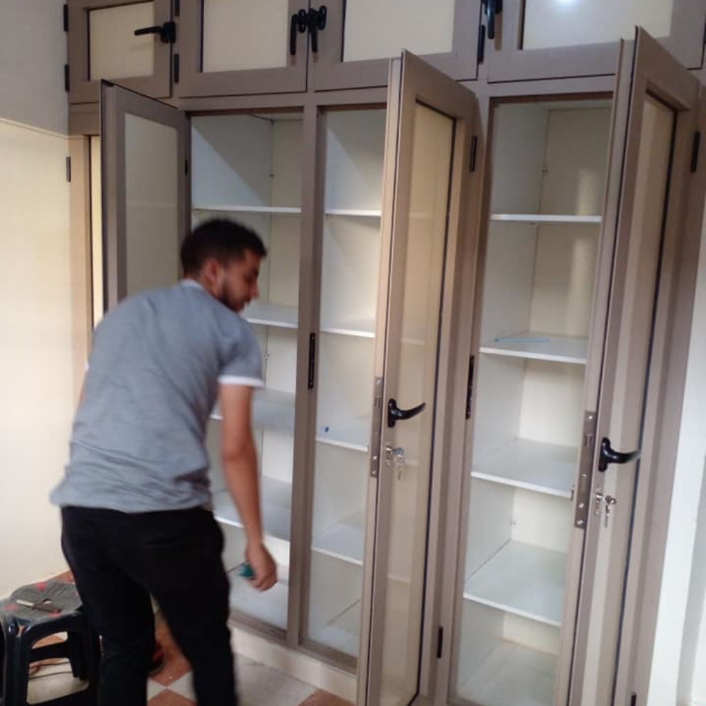 عامل يقوم بتركيب خزانة ألمنيوم حديثة بلون رمادي فاتح مع أبواب زجاجية شفافة.